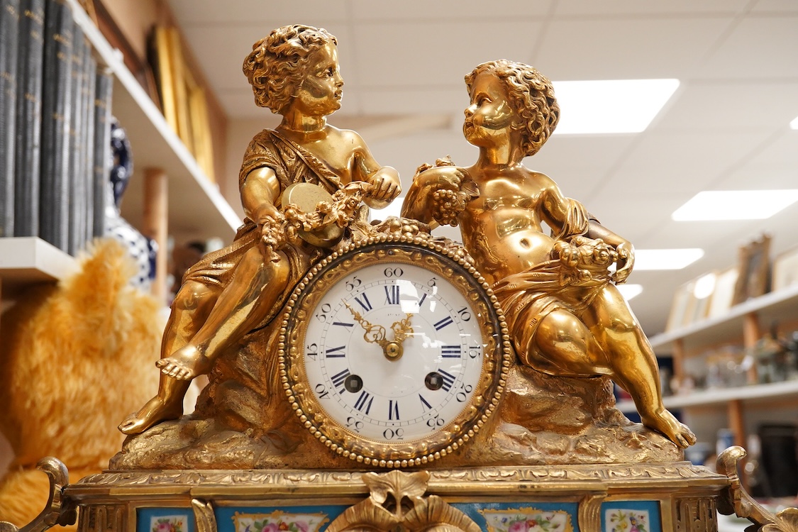A Louis XV style figural brass mantel clock striking on a bell, with enamel dial and inset plaques, surmounted with two figures, with pendulum, no key, 42cm wide
